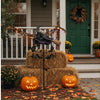 A decorative witch wind rotor with a wreath hanging on a porch decorated for Halloween.