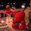 Un ours rose en peluche avec un ruban noir et une décoration lumineuse LED sur une table.