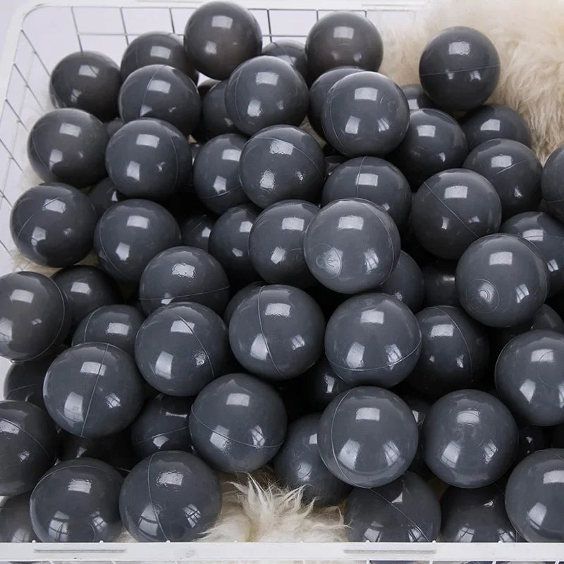 A large quantity of dark gray and black spherical balls for kids' play areas is displayed in a white basket.