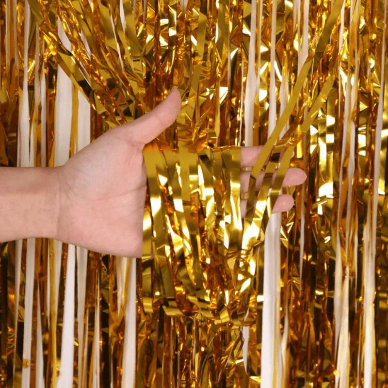 A hand is reaching through a curtain made of metallic gold and white foil fringe.