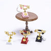 A vintage rotary desk phone miniature decor with gold and pink accents displayed on a wooden stand.