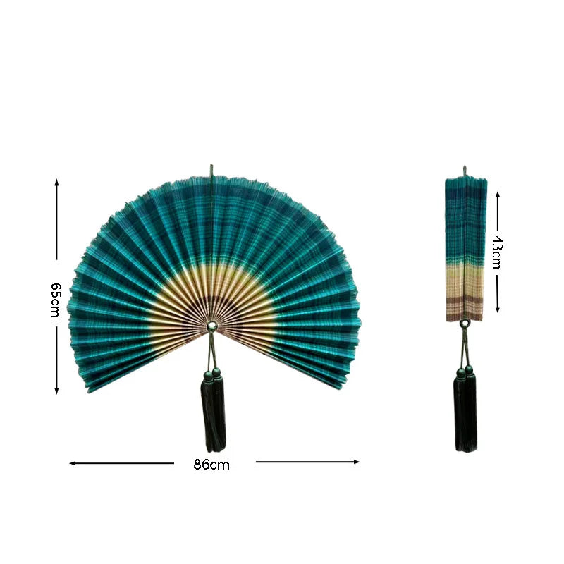 Handwoven bamboo wall fan decor in teal and gold with a black tassel.