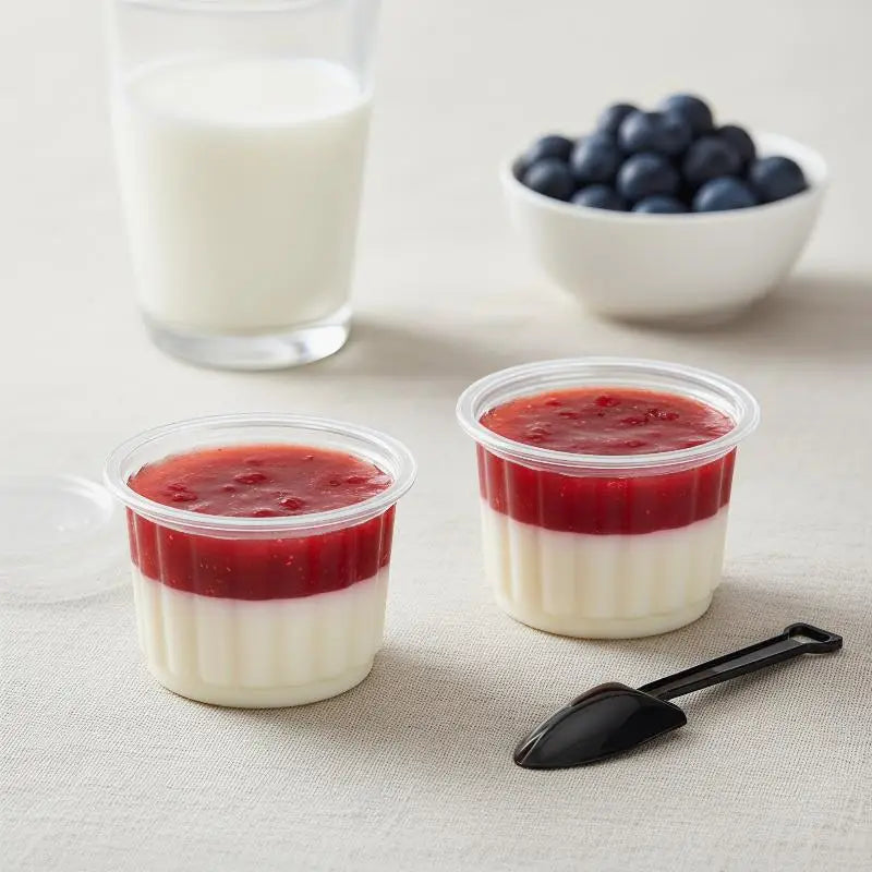 Three clear disposable dessert cups with lids containing layered red and white desserts next to a glass of milk and blueberri