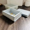 A white openable book-shaped silicone mold for resin and concrete DIY with gold-colored items inside.