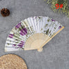 A hand carved bamboo folding fan with a floral and greenery pattern is displayed on a gray surface.