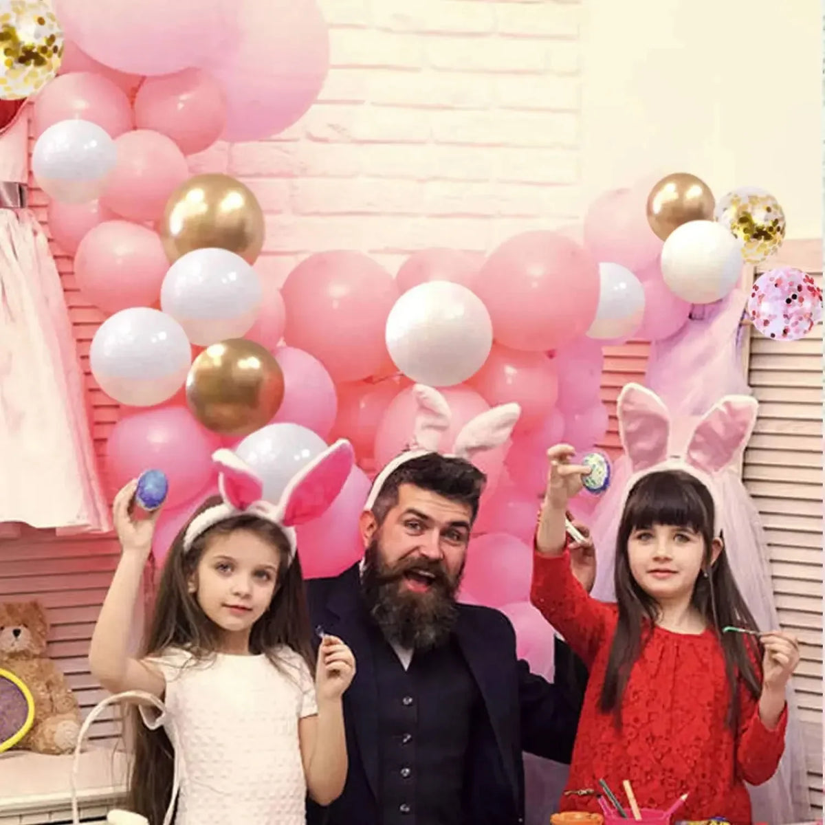 A family portrait featuring a father and two daughters posing with pink and gold latex balloons.