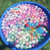 A blue bowl filled with numerous water balloons in various shades of pink, purple, and green.