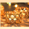 A close-up of a set of gold crystal votive candle holders glowing warmly on a surface.