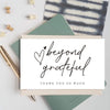 A stack of white thank you cards with black script reading beyond grateful resting on a green card and scattered wooden items