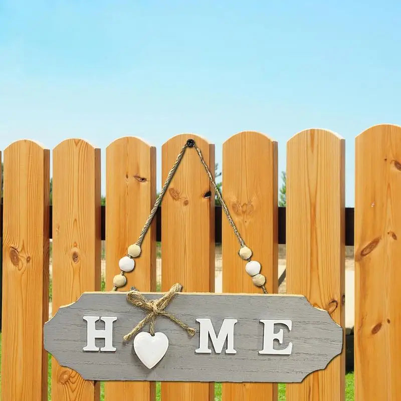 A wooden welcome sign with the word HOME carved into it, hanging on a rustic fence.