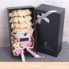 A dark gift box containing a bouquet of cream and peach roses wrapped in natural straw and pink paper