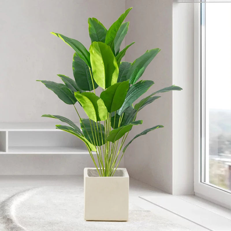 Artificial tropical palm tree with large green monstera leaves potted in a white square planter