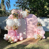 A pink and gold balloon garland arch display featuring various sized balloons and confetti on a wooden surface.