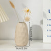 A minimalist ceramic vase with a textured finish holds dried floral elements on a white shelf.