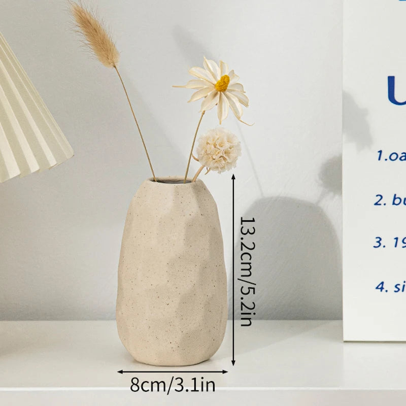 A minimalist ceramic vase with a textured finish holds dried floral elements on a white shelf.