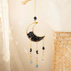 A gold-toned moon-shaped crystal suncatcher with black beads and dangling rainbow prisms.
