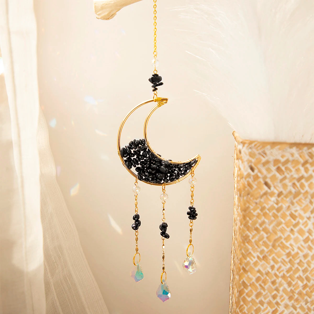 A gold-toned moon-shaped crystal suncatcher with black beads and dangling rainbow prisms.