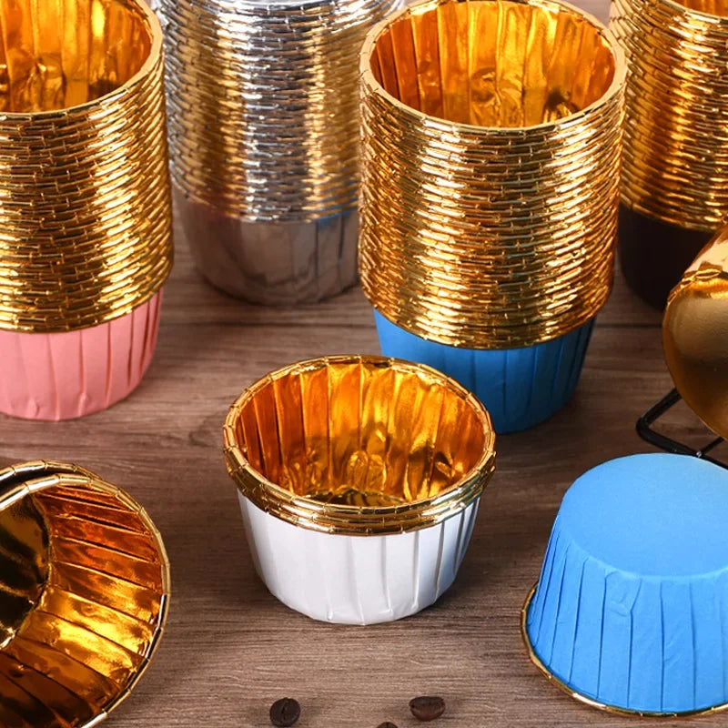 A collection of shiny gold greaseproof cupcake liners in various sizes and colors are displayed on a wooden surface.