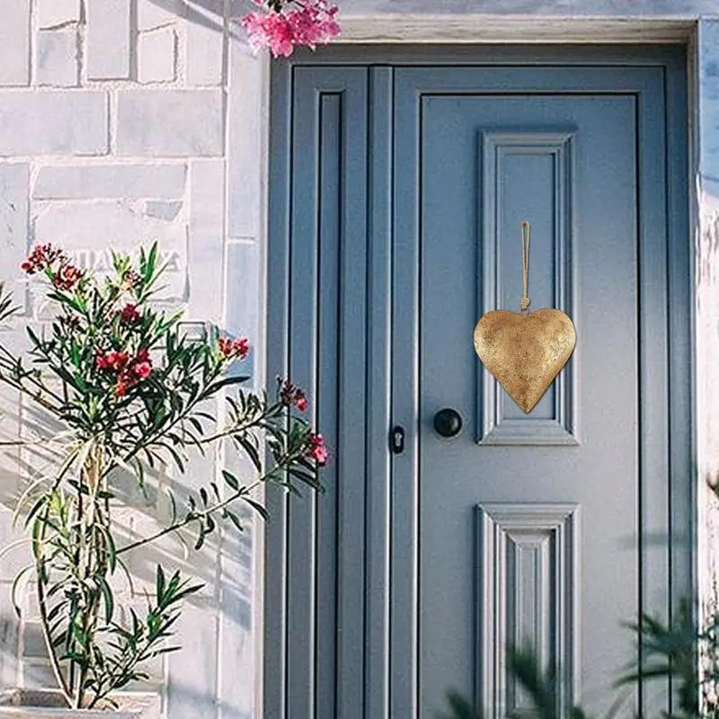 A light blue wooden door with a gold heart decoration and greenery in the foreground.
