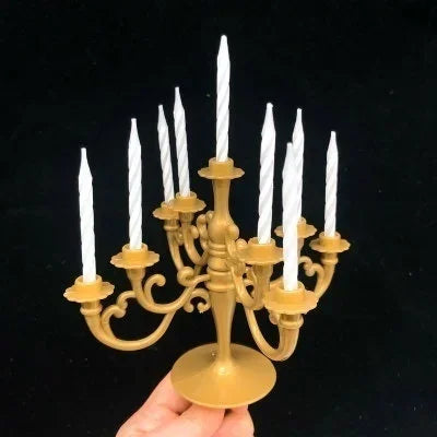 A set of nine white birthday cake candles with gold holders displayed in a hand.