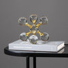 A minimalist sculpture of gold-toned molecular structures made of clear glass resting on a white book.