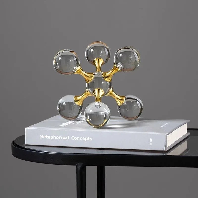 A minimalist sculpture of gold-toned molecular structures made of clear glass resting on a white book.