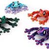 Three articulated 3D printed frog magnets in blue, green, and purple showing various grips.