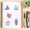 A spiral notebook page featuring various colorful crystal and gemstone stickers on white paper.