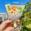 A bouquet of handcrafted crochet flowers in orange and white colors is held against a bright blue sky.