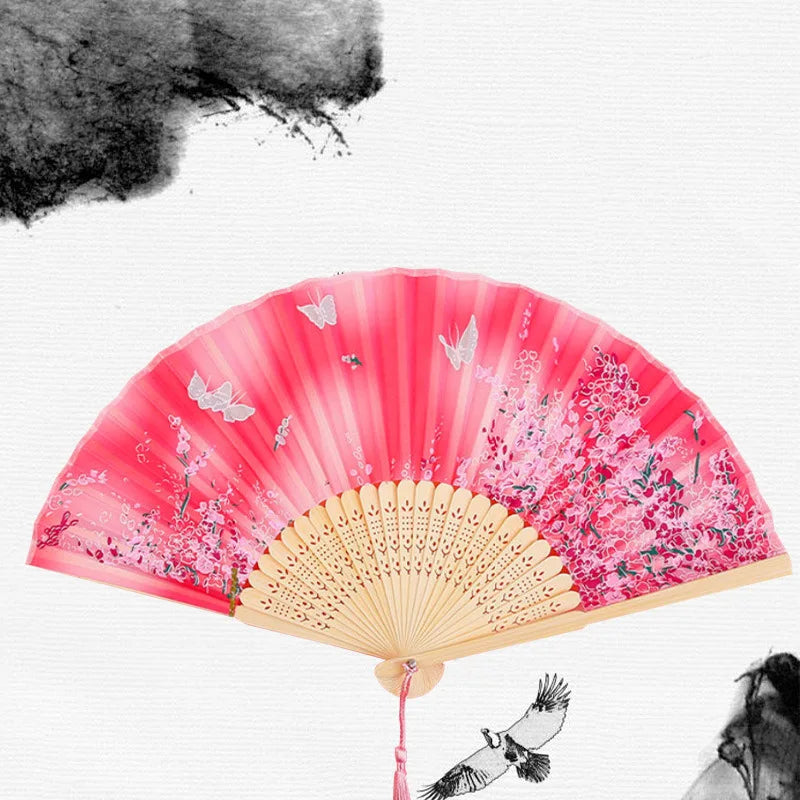 A pink and white vintage bamboo folding hand fan with floral accents against a white background.