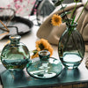 A set of three clear glass mini vases with a greenish tint displayed on a dark book.