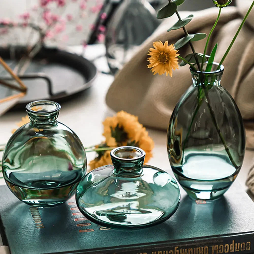 A set of three clear glass mini vases with a greenish tint displayed on a dark book.