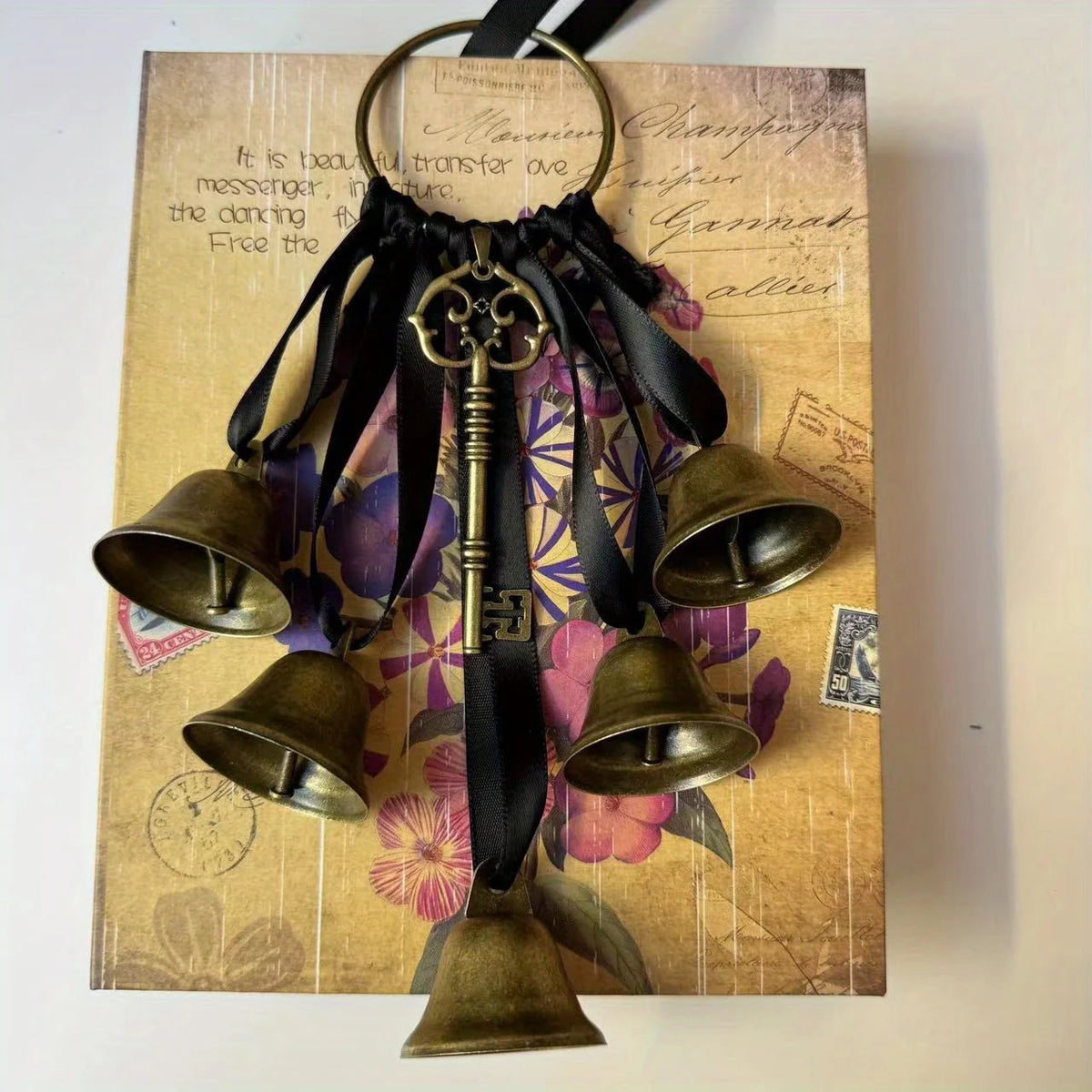 Decorative metal wind chimes hanging from a black ribbon on aged paper