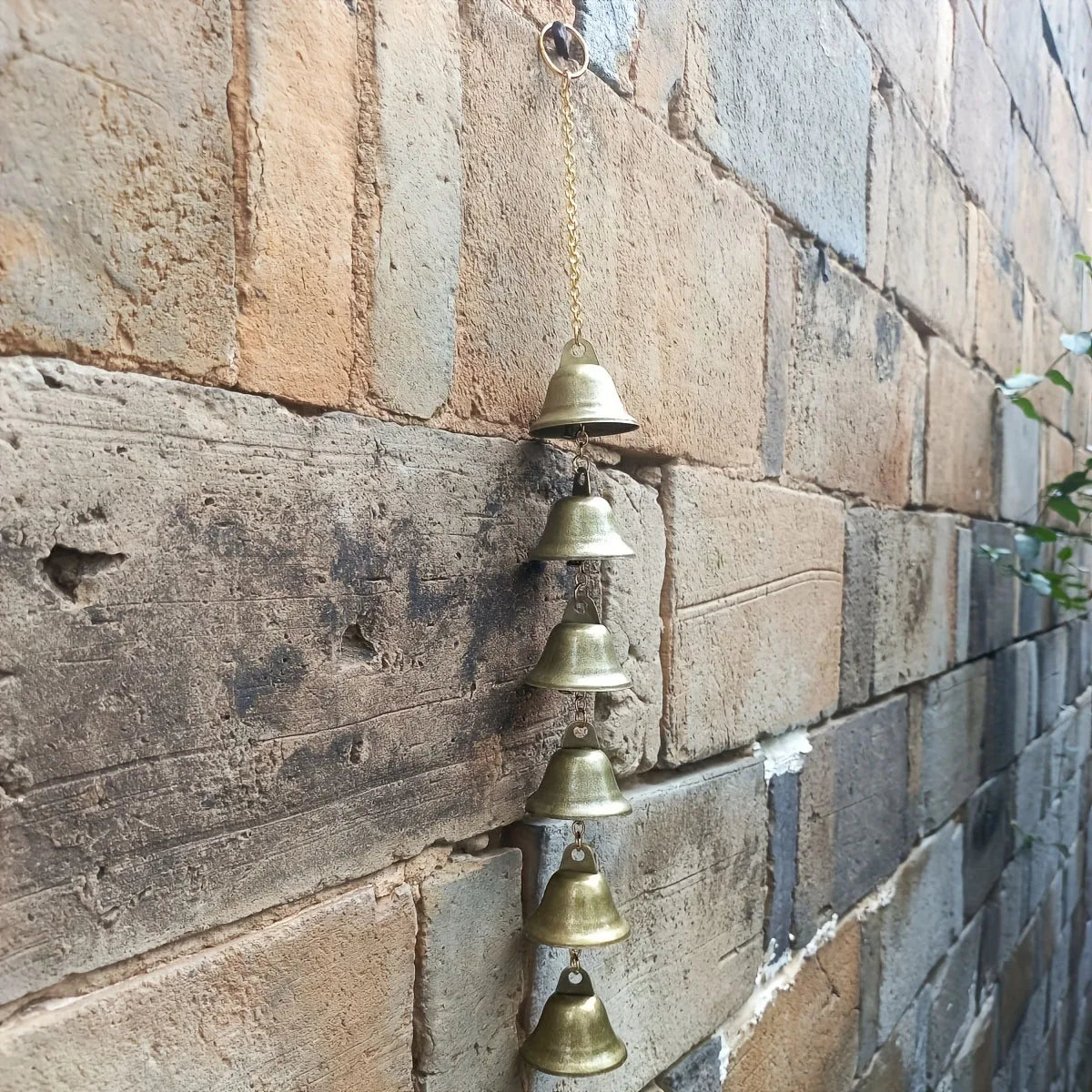 A vertical arrangement of brass metal wind chimes hanging on a textured stone wall.