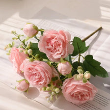 A bouquet of pink silk peony roses and buds arranged on white paper.