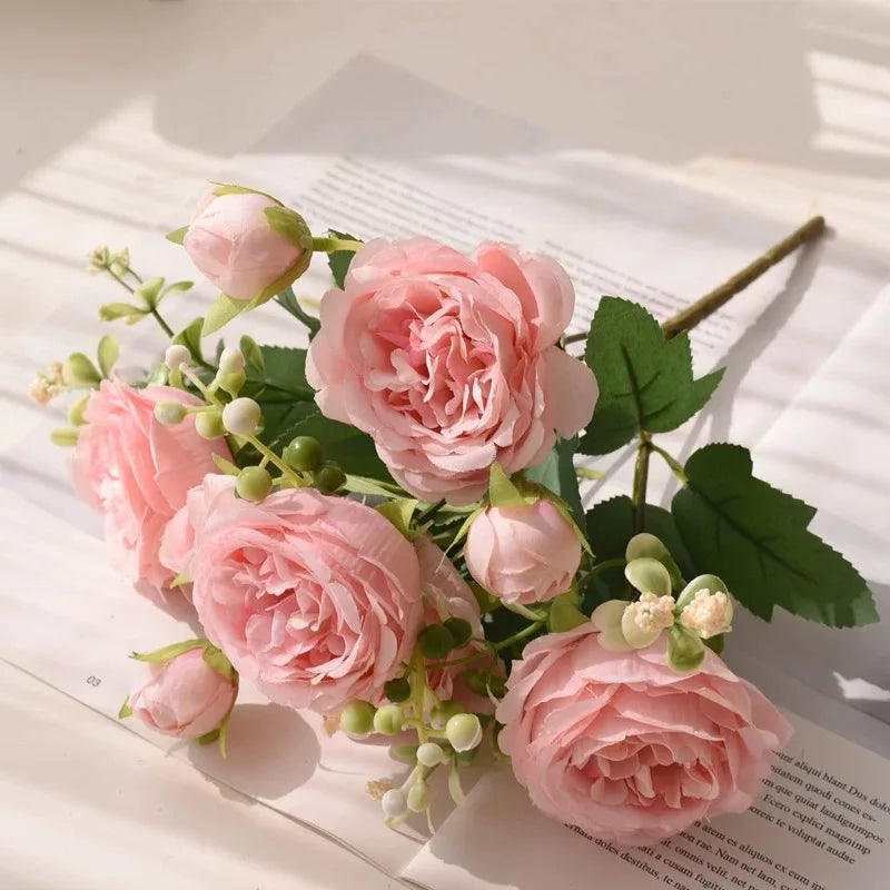 A bouquet of pink silk peony roses and buds arranged on white paper.