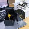 Une boîte cadeau noire avec un geste de la main en or, posée sur un ordinateur portable argenté.