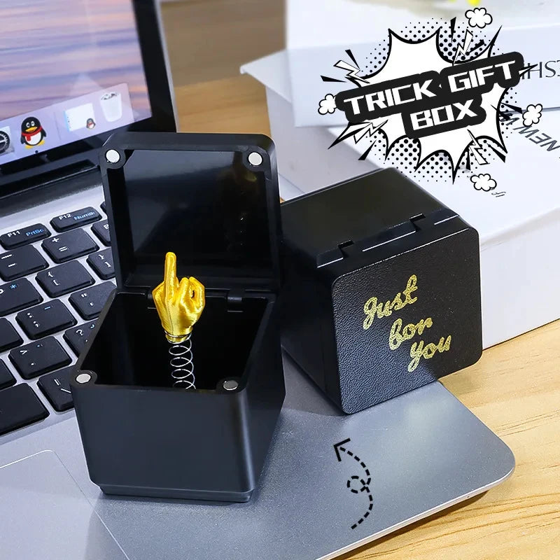 Une boîte cadeau noire avec un geste de la main en or, posée sur un ordinateur portable argenté.