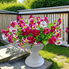A vibrant bouquet of artificial silk pink and white flowers in a white pedestal vase set on an outdoor deck.