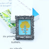 A miniature framed piece of art featuring a yellow tree against a light blue background.