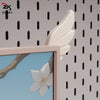 A close-up view of a light pink monitor wing decoration with white, stylized feathers against a patterned wall.