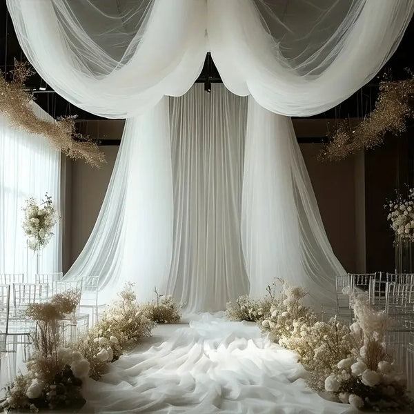 Elegant white sheer fabric drapes hanging from the ceiling creating a soft, flowing backdrop for an event.