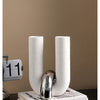 Two tall, cylindrical ceramic ornaments in white and silver are displayed on a dark surface.