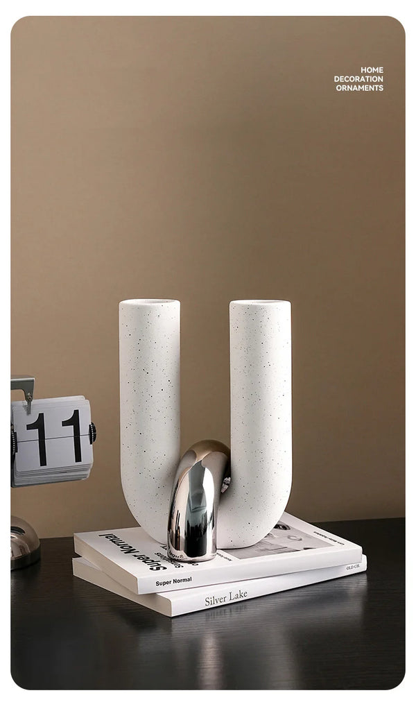 Two tall, cylindrical ceramic ornaments in white and silver are displayed on a dark surface.