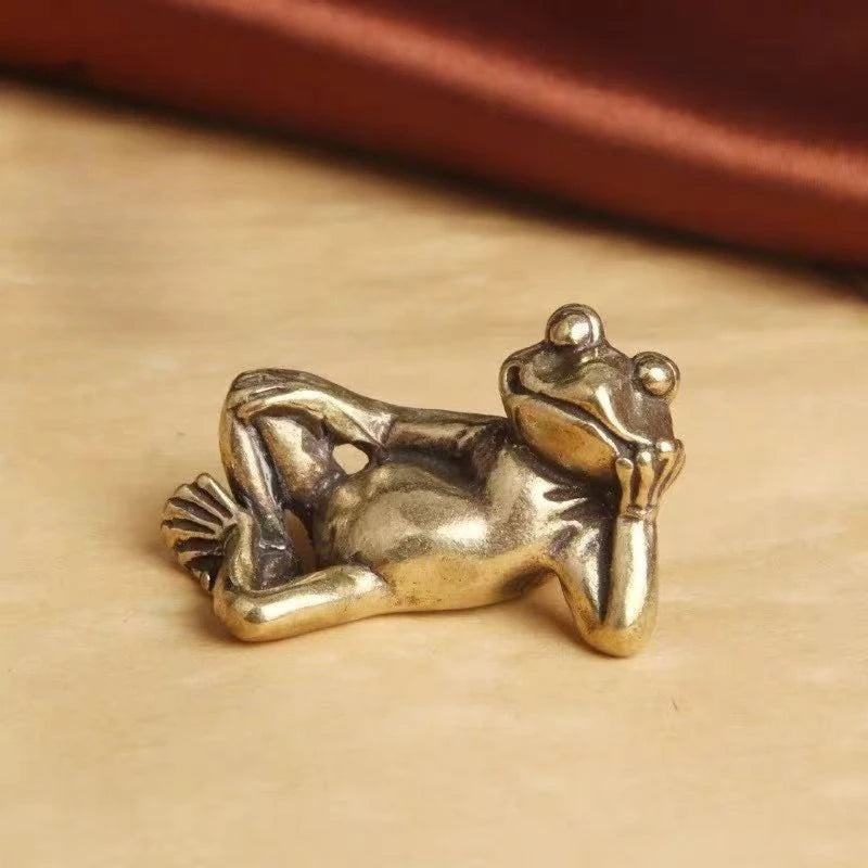 Antique brass sleeping frog figurine resting on a light surface.