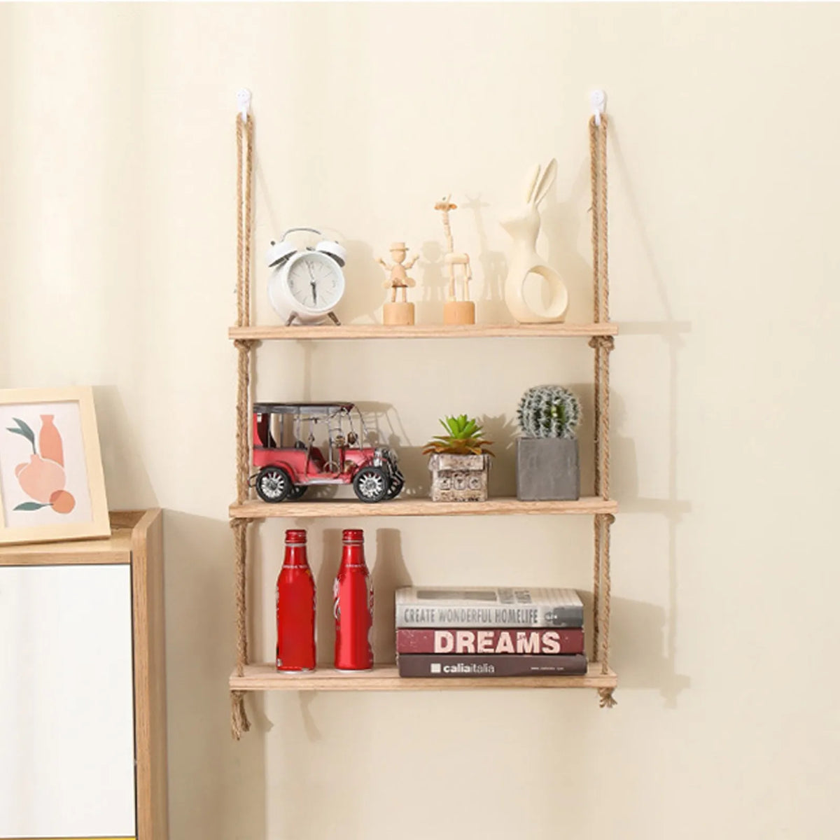 Rustic wooden hanging shelves with rope displaying various decorative items and books on a light wall.