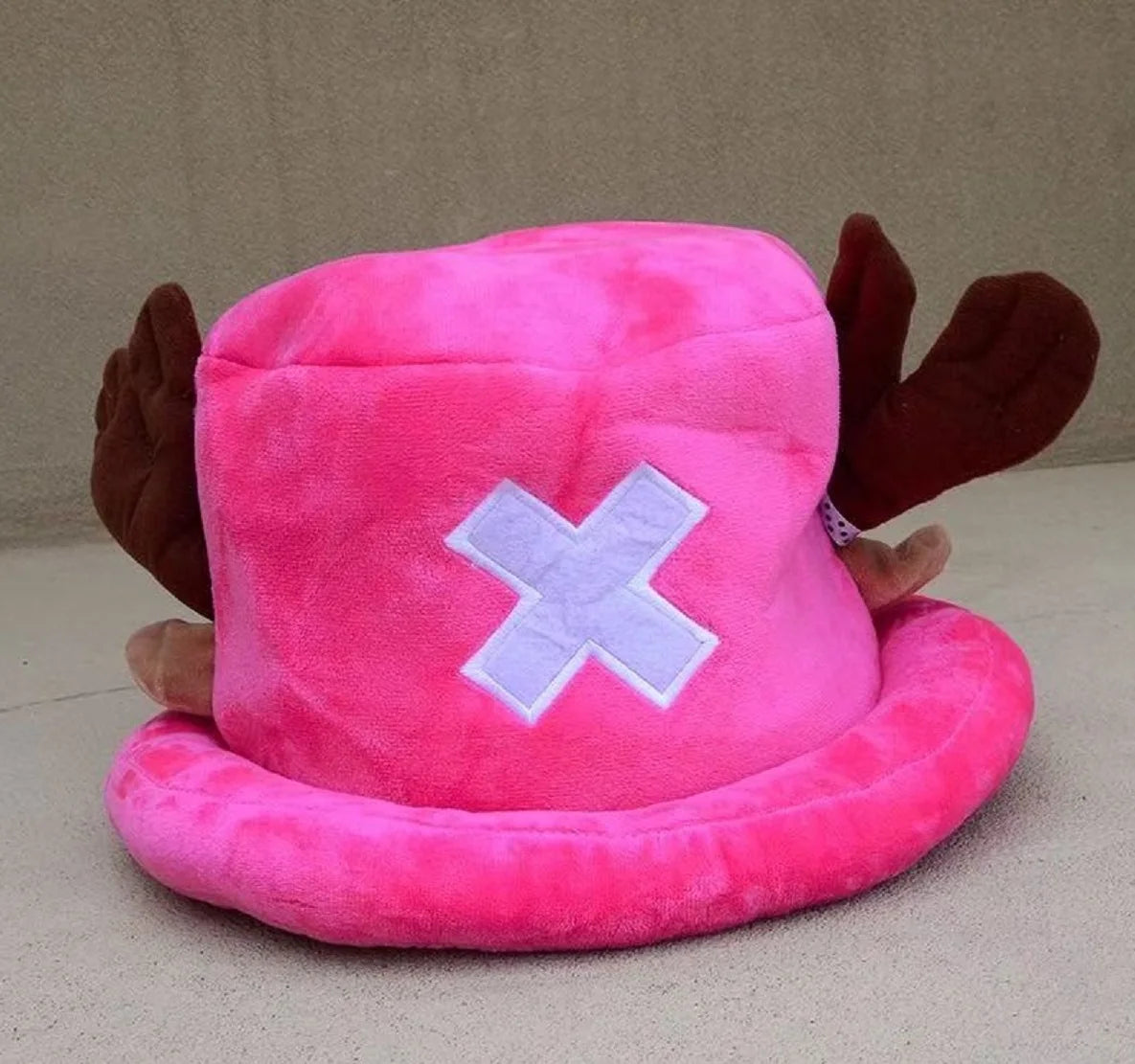 A pink plush knit cap featuring a white cross design and brown ear accents.