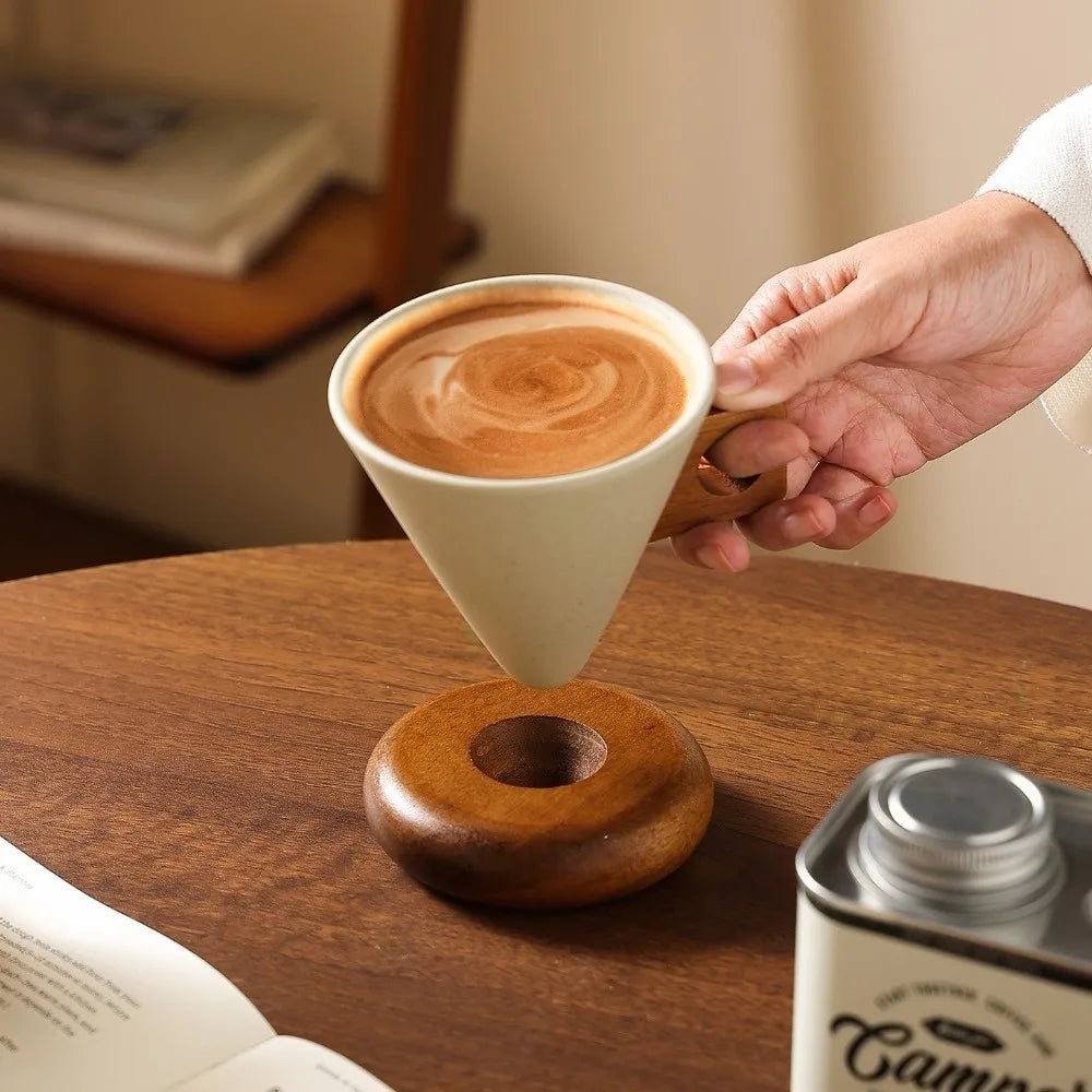A hand is pouring coffee into a ceramic mug resting on a wooden base.