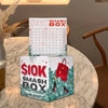 A stack of $10K Smash Box acrylic budget planning money boxes on a marble table.