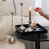 A set of three silver waterdrop design candle holders with a lit candle on a black tray